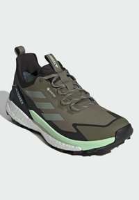 Zapatilla de trail running en verde y negro con parte superior texturizada, cierre de cordones, media suela acolchada y suela exterior con tracción prominente. Diseño impermeable.