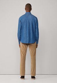 Lichtblauw denim overhemd met een button-down kraag en lange mouwen. Gecombineerd met beige corduroypants met een relaxte pasvorm.