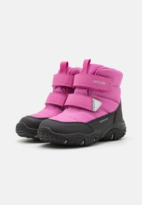 Bottes imperméables roses avec semelles en caoutchouc noir, équipées de sangles Velcro, d'un support de cheville rembourré et d'une texture de grip pour une adhérence optimale.