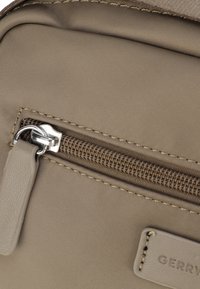 Borsa in tessuto beige con una superficie liscia, dotata di una cerniera orizzontale e di un'etichetta in pelle rettangolare con la scritta "GERRY". Cuciture visibili lungo i bordi.