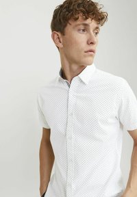 Camicia a maniche corte, con bottoni, in tessuto bianco con un motivo sottile di piccole croci scure; presenta un colletto standard e una vestibilità rilassata.