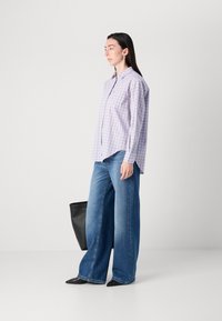 Light purple checkered button-down shirt with long sleeves, paired with wide-leg blue jeans and black pointed-toe flats, holding a black tote bag.