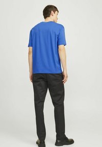 Mėlynas medvilninis marškinėliai su apvaliu kaklu, trumpomis rankovėmis ir tiesiu kirpimu, derinami su juodomis kelnėmis ir juodais batais.