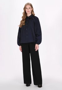 Camicia button-up oversize di colore blu navy con colletto e maniche a sbuffo, abbinata a pantaloni a gamba larga neri a vita alta. Tessuto morbido.