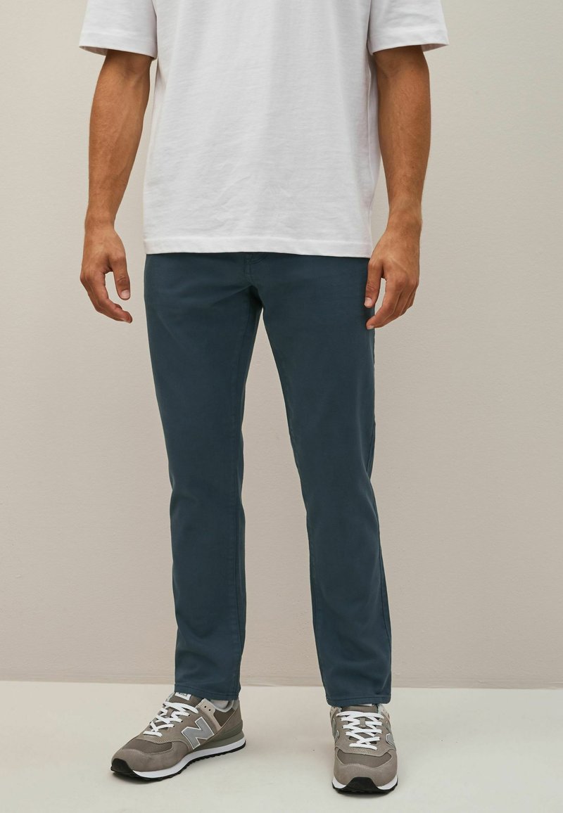 Pantaloni din bumbac de un albastru deschis, cu o croială slim, având o textură netedă. Asortați cu adidași gri și albi, cu șireturi și detalii cu logo.