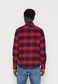 Camicia flanella a quadri rossi e blu navy con maniche lunghe, polsini con bottoni e orlo dritto, caratterizzata da un collo classico e una texture morbida.