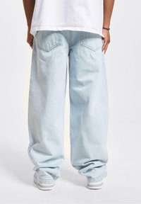 Lyseblå baggy jeans laget av denim, med løs passform, oppbrettede hems og baklomme. Kombinert med hvite sneakers.