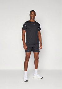 Must sportlik t-särk valgete aktsentide ja logoga; mustad lühikesed püksid; valged sokid; ja tossud musta tallaga. Sile kangas, liibuv disain.