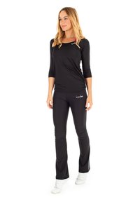 Black long-sleeve top and black fitted pants made of stretchy material. The top features a round neckline and front logo detail.