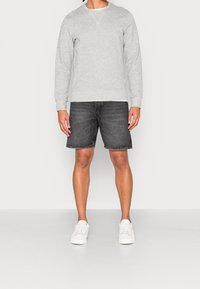 Sudadera gris de manga larga, con cuello redondo, llevada sobre una camisa blanca, combinada con pantalones cortos de mezclilla oscura y zapatillas blancas.
