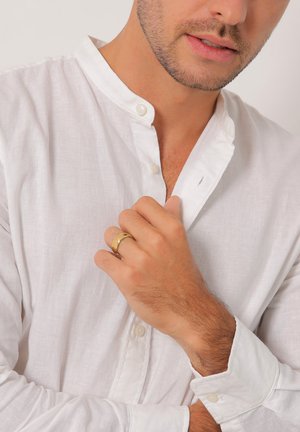 White linen shirt with a mandarin collar and buttoned closure. A gold ring is worn on the hand, highlighting skin texture and simple design.