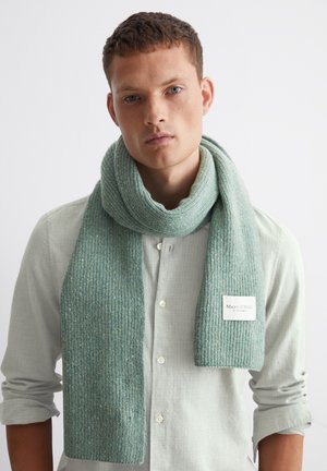 Light green knitted scarf with ribbed texture and a tag reading "Marc O'Polo." Worn casually over a checkered shirt.