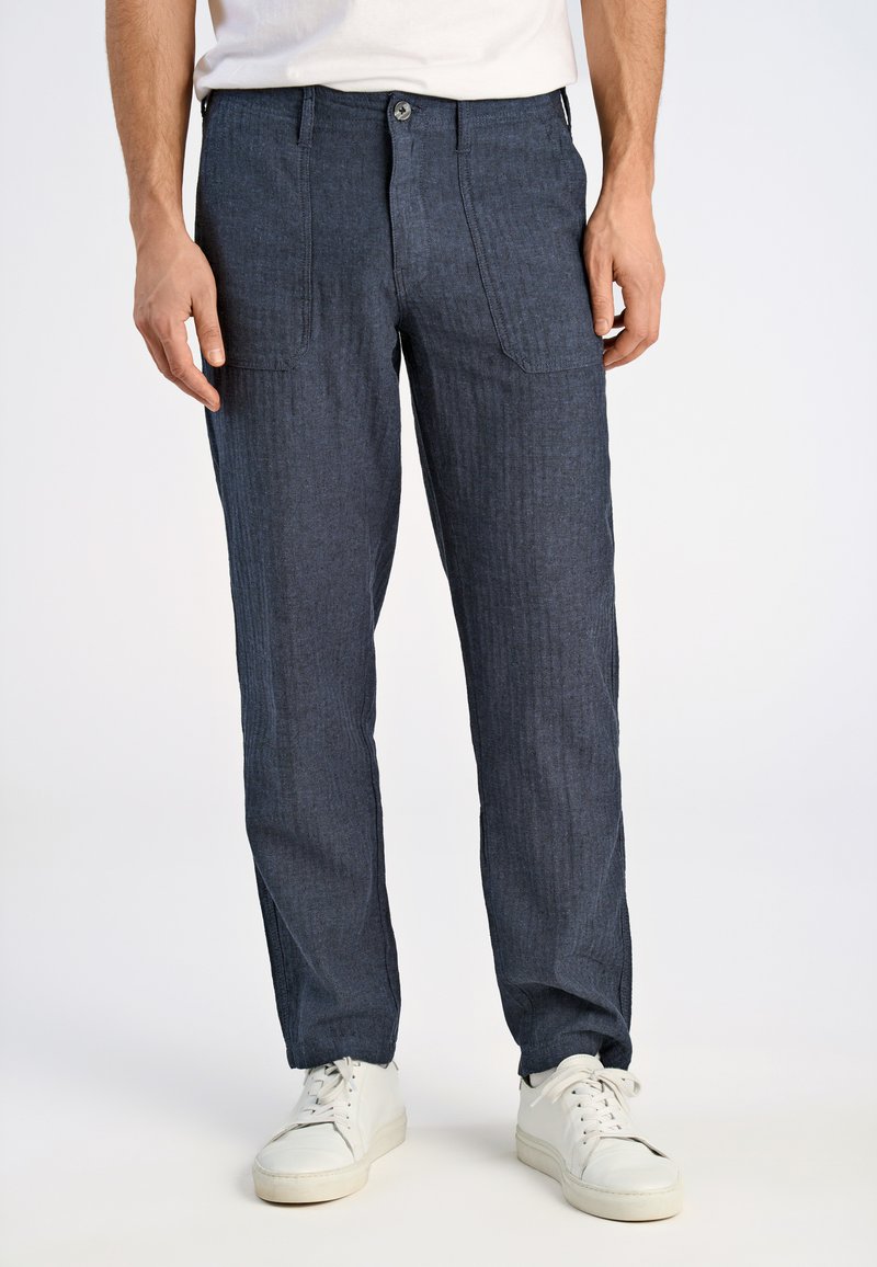 Mörkblå randiga byxor i ett lättviktigt material, med framfickor och knäppning, ihopparade med vita sneakers.