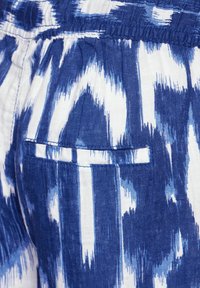 Ikat-mönstrad tyg i blått och vitt, med en sidoficka med en smal trim. Texturen verkar lätt och vävd.