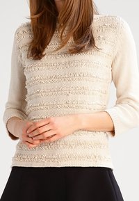 Top in misto beige con strisce arricciate testurizzate, maniche a tre quarti e design aderente. Tessuto morbido e liscio con dettagli delicati.