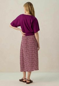 Haut violet à manches courtes associé à une jupe fleurie longueur genoux dans des nuances de bordeaux et de rose. Des sandales marron complètent le look.