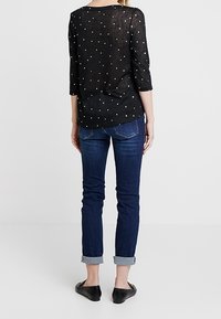 Svart, lätt blus med trekvartsärmar och vita prickar; ihop med rullade mörkblå jeans och svarta platta skor.