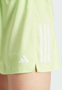 Light green athletic shorts made of smooth fabric, featuring white three-stripe design and logo, with side slits for added movement.