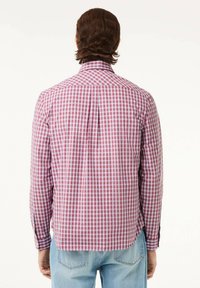 Camisa de cuadros en rojo y blanco con mangas largas, cuello botonado y pliegue en la parte posterior, combinada con jeans de color azul claro.