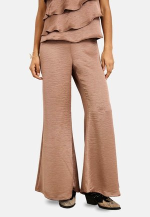 Mujer con pantalones marrones texturizados de tiro alto y pierna ancha combinados con zapatos de tacón estampados en negro y beige.