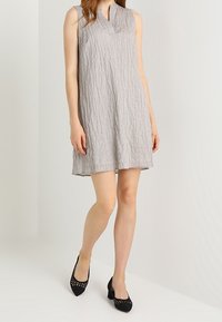 Vestido de lino gris sin mangas con un acabado texturizado, que presenta un escote en V y una silueta ligeramente acampanada. Combina con tacones negros perforados.