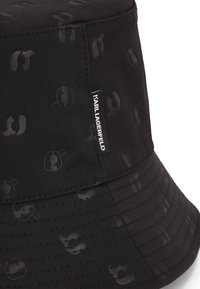 Cappello a secchiello nero realizzato in tessuto testurizzato, con un discreto motivo logo tono su tono e un'etichetta laterale con il marchio "Karl Lagerfeld".