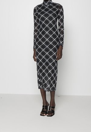Schwarzes transparentes Midikleid mit weißem diagonalem Karomuster, langen Ärmeln, hohem Kragen, kombiniert mit schwarzen Riemchen-Sandaletten mit Absatz.