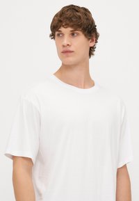 Vit bomull T-shirt med kort ärm, rundad halsringning och avslappnad passform. Slät textur utan synliga mönster eller detaljer.
