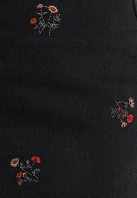 Svart tyg med små broderade blommönster i rött, rosa och orange utspridda över ytan.