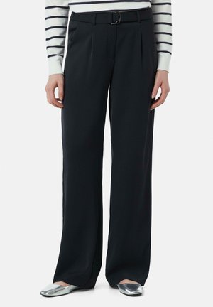 Zwarte wijde broek van een soepele stof met plooien, voorzien van een riem met een zilveren gesp, gecombineerd met metallic platte schoenen.