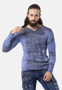 Langärmliges blaues T-Shirt mit V-Ausschnitt, das ein gemustertes Design und drei dekorative Knöpfe nahe dem Ausschnitt aufweist.