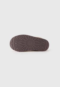 Brown rubber sole of a shoe with a sunburst and zigzag tread pattern, photographed against a plain white background.