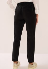 Zwarte tapered broek met een elastische tailleband, voorzien van twee achterzakken en geribde boorden. Gepaard met beige lage sneakers.