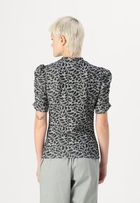 Top cinza com mangas bufantes, apresentando um padrão de folhas pretas e um design de gola alta. O material parece leve com um acabamento texturizado.