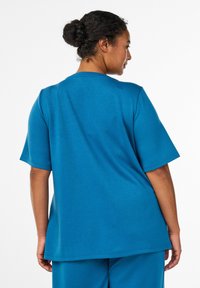 Tričko s krátkým rukávem v tyrkysové barvě s volnějším střihem. Měkká textura, kulatý výstřih a mírně zakřivený lem. Doplněno kalhotami ve stejné barvě.