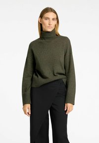 Dunkelgrüner Strickrollkragenpullover mit lockerer Passform, gerippten Bündchen und Saum. Kombiniert mit schwarzen, hochtaillierten, weit geschnittenen Hosen.