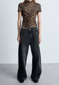 Top ajustado de manga corta con estampado de leopardo, combinado con jeans amplios de pierna ancha en un tono oscuro. Tejido texturizado, brillo sutil y cinturilla alta.