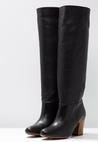 Bottes en cuir noir jusqu'au genou avec une finition texturée, dotées d'un bout rond et d'un talon en bloc de bois. Design supérieur lisse.