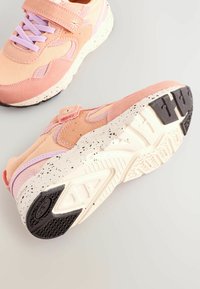 Sko med en overdel i pink og ferskenfarvet stof, med lavendel detaljer og en velcro-lukning. Hvid sål med sorte gummisektioner og stænk.