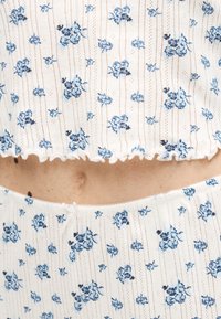 Λευκό ριμπ ύφασμα με μικρό μπλε λουλουδένιο σχέδιο σε ταιριαστό κοντό τοπ και σορτς, που δείχνει τη μέση και τον αφαλό με ανοιχτόχρωμο δέρμα.