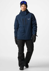 Navy waterproof jacket with a hood, two chest pockets, and zipper closures, paired with black pants and gloves. Features snow goggles.