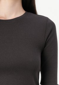 Dunkelgraues Langarmshirt mit rundem Ausschnitt, aus strukturierter Stoff gefertigt, das eine glatte Textur und eine figurbetonte Passform präsentiert.