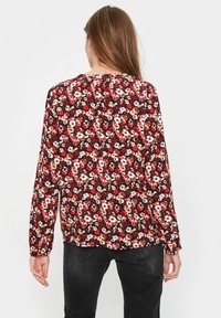 Blus med lång ärm som har ett rödblommigt mönster med vita och gula accenter. Gjord av lättviktsmaterial med avslappnad passform och rundad nederkant.