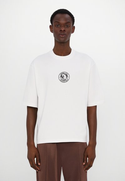 Witte T-shirt met korte mouwen van katoen, met een ronde halslijn en een centraal cirkelvormig logo in het zwart. Eenvoudige, relaxte pasvorm.