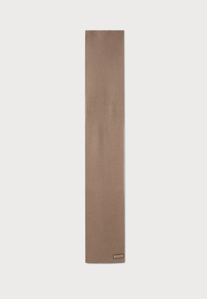 Lang beige ribstrikket tørklæde med et lille rektangulært mærke nær den ene ende, vist på en enkel lys baggrund.