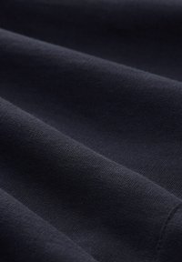 Detailní záběr tmavě modré látky s viditelnou pletenou strukturou a jemnými sklady vytvářejícími jemné stíny.