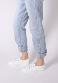 Weiße Leder-Sneaker mit abgerundeten Zehen, silbernen Ösen und dezenten Herzverzierung. Kombiniert mit hellblauen Jeans mit umgeschlagenen Hosenbeinen.