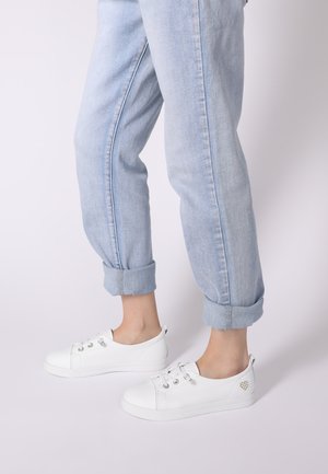 Weiße Leder-Sneaker mit abgerundeten Zehen, silbernen Ösen und dezenten Herzverzierung. Kombiniert mit hellblauen Jeans mit umgeschlagenen Hosenbeinen.