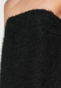 Κοντινή λήψη από τον ώμο και το άνω μέρος του στήθους ενός ατόμου καλυμμένα με ένα μαύρο ρούχο με υφή αφράτου υφάσματος.