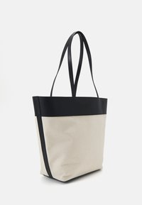 Sac fourre-tout avec un haut en simili cuir noir et un corps en toile crème. Dispose de deux longues poignées et d'une forme structurée. Accentué par des détails de couture.
